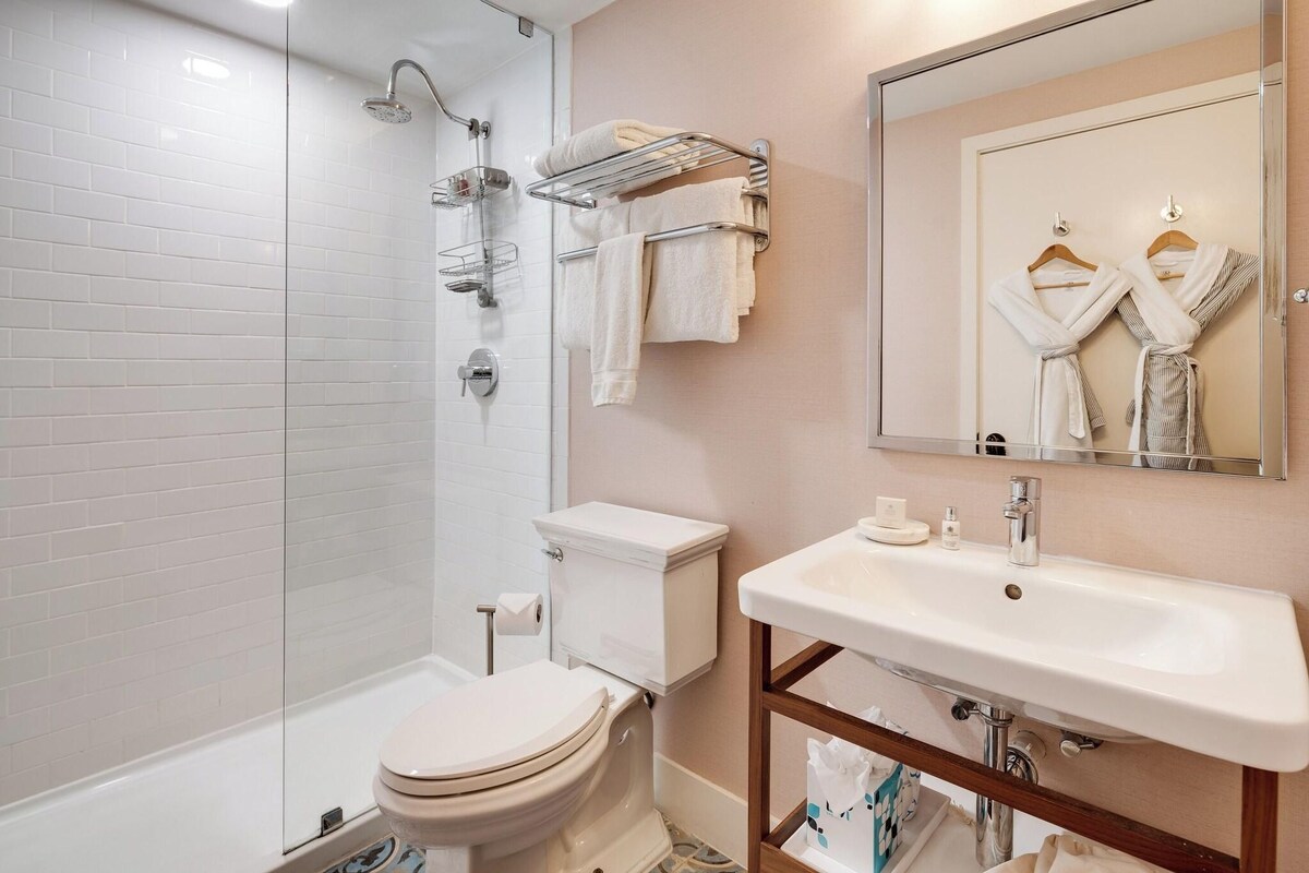 A bathroom with a toilet, shower, sink, and towel rack.