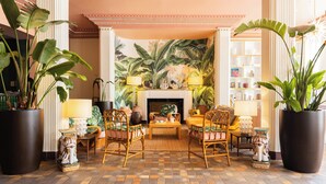 A spacious living room with a fireplace, large potted plants, wicker furniture, and a tropical mural on the wall. - The Savoy Hotel & Beach Club (Miami Beach)