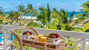 A breakfast tray with fruits, juices, and eggs on a balcony overlooking a beach with palm trees and a pool. - The Savoy Hotel & Beach Club (Miami Beach)