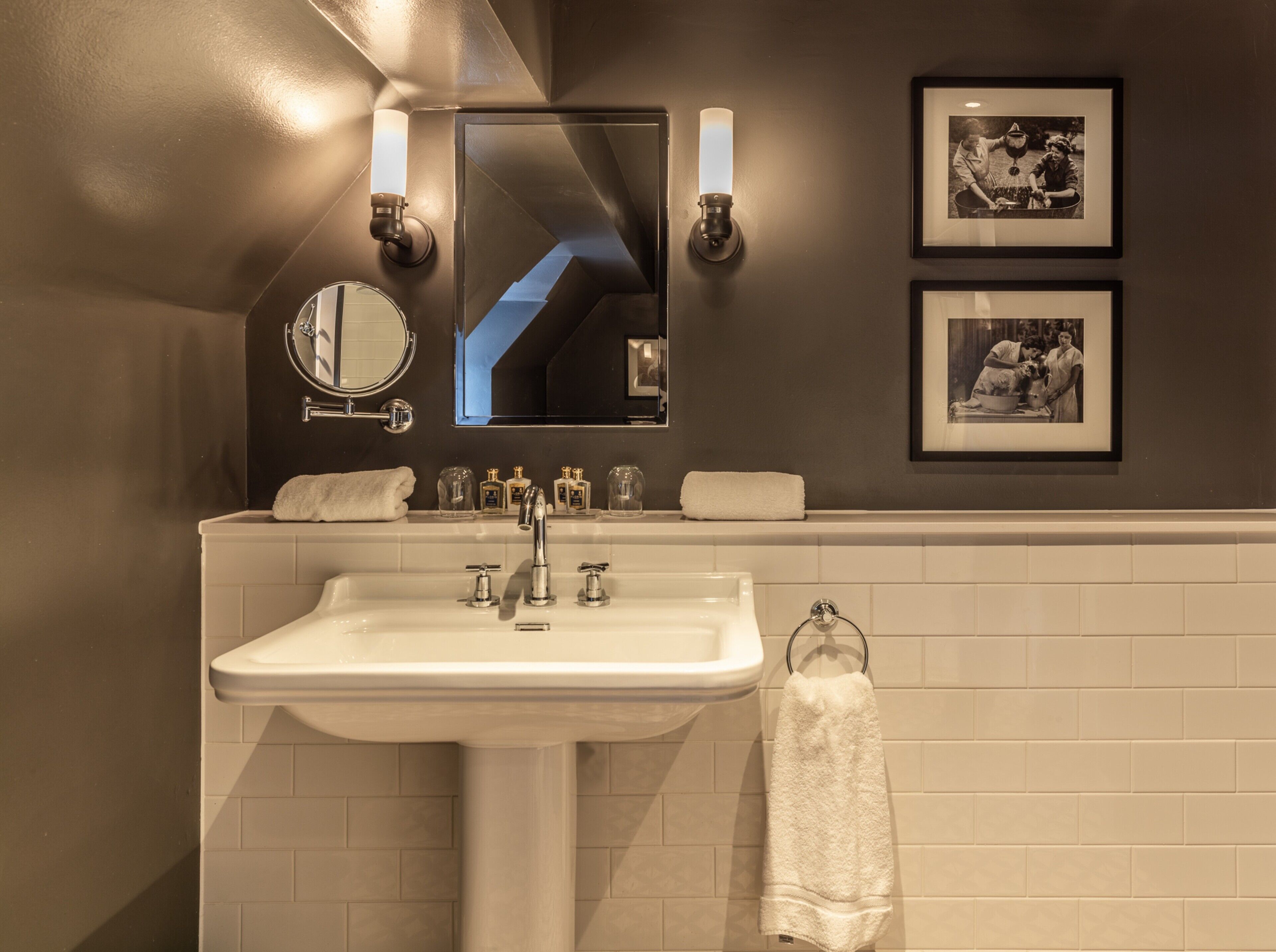 A modern bathroom with a white sink, two wall-mounted lights, a mirror, and two framed photographs on the wall.