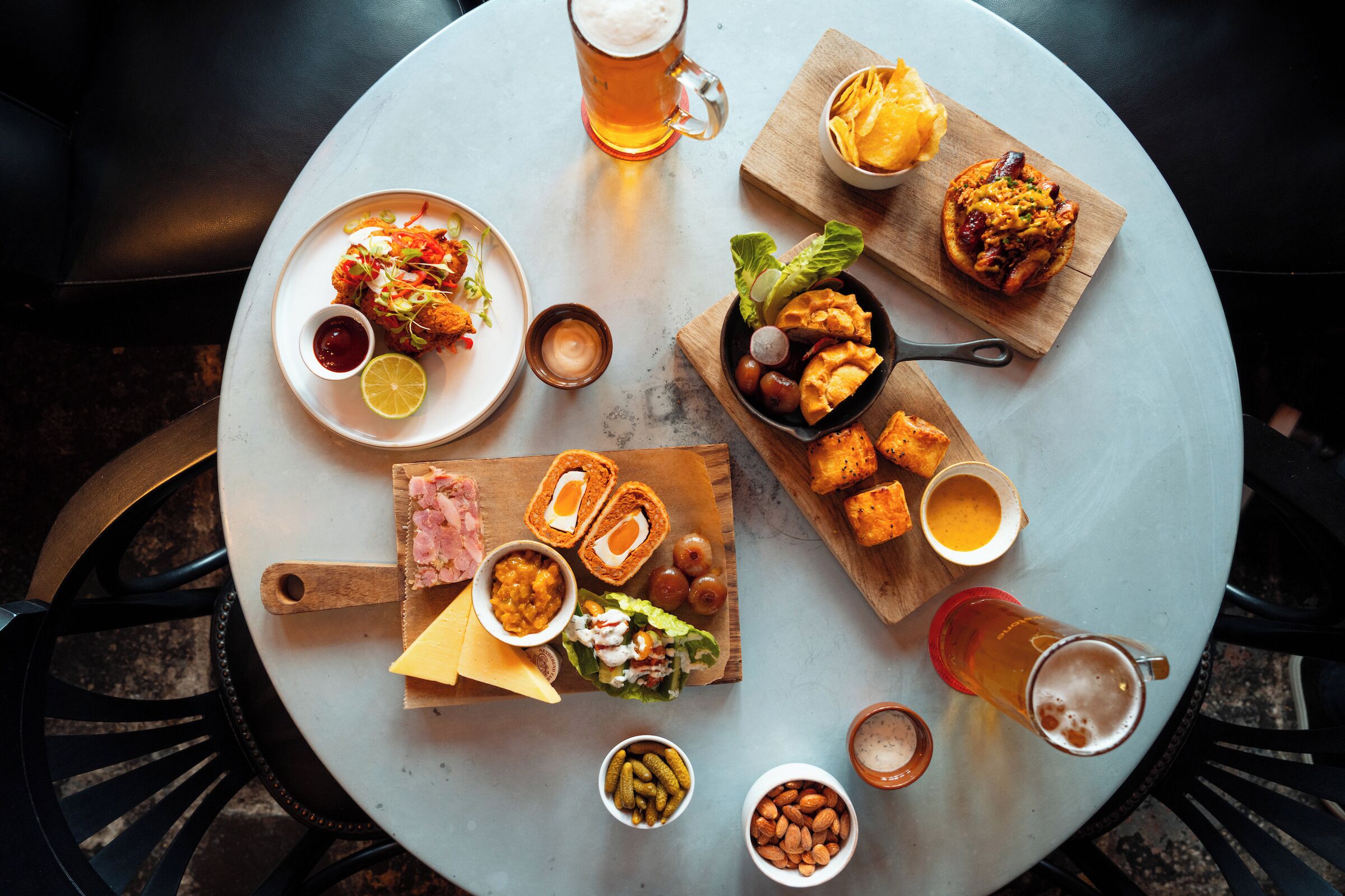 A round table with various food items and drinks, including a plate of fried chicken, a bowl of salad, and a mug of beer.