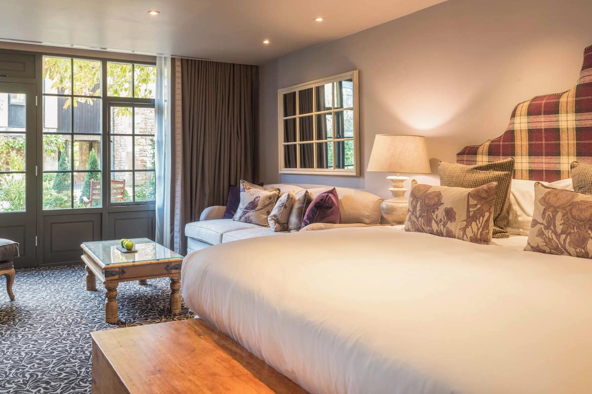 A hotel room with a large bed, a sofa, a coffee table, and a view of the outdoors through large windows.