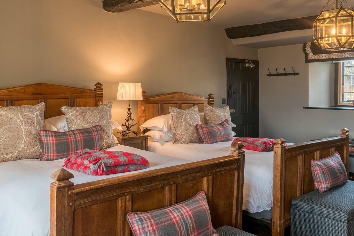A traditional bedroom with two wooden beds, patterned pillows, a nightstand with a lamp, and a hanging lantern.