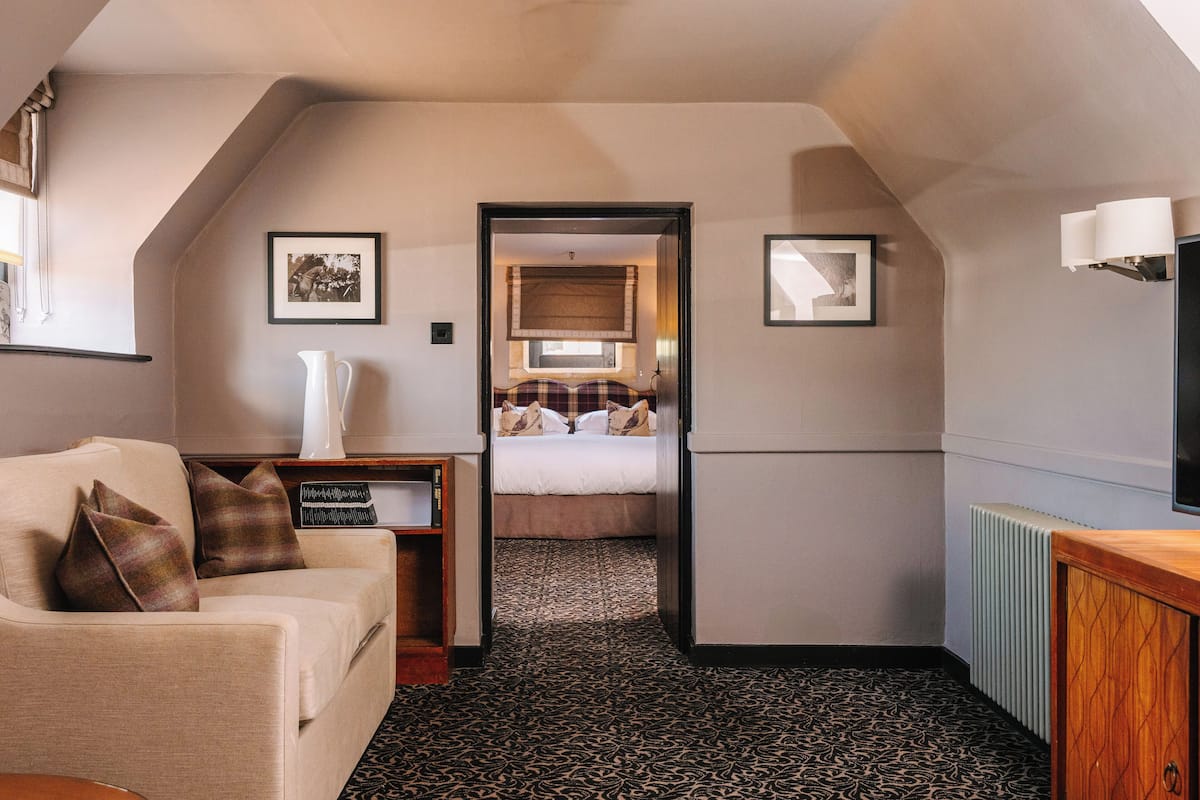 A hotel room with a sofa, a bed, a small table, a radiator, and framed pictures on the walls.