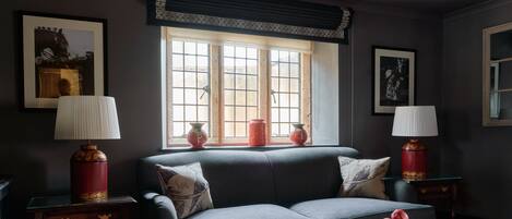 A cozy living room with a grey sofa, two side tables with lamps, a window with curtains, and a red patterned carpet.