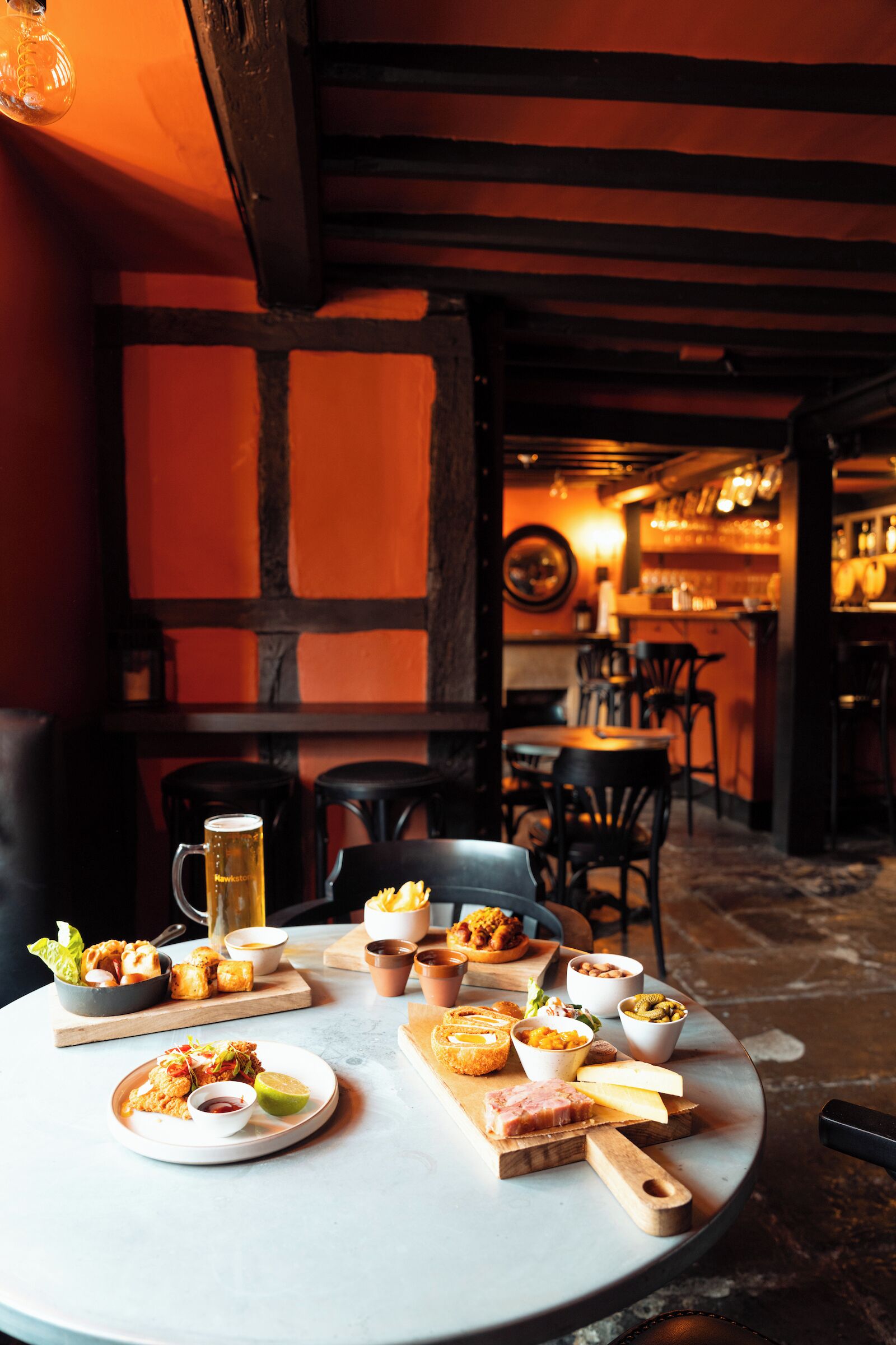 A dining table with various dishes, a beer mug, and a bar area in the background.
