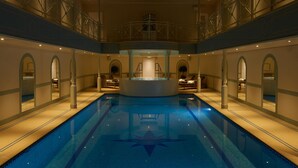 Une piscine intérieure dotée d’une plateforme circulaire centrale, entourée d’espaces de détente et d’arcades.