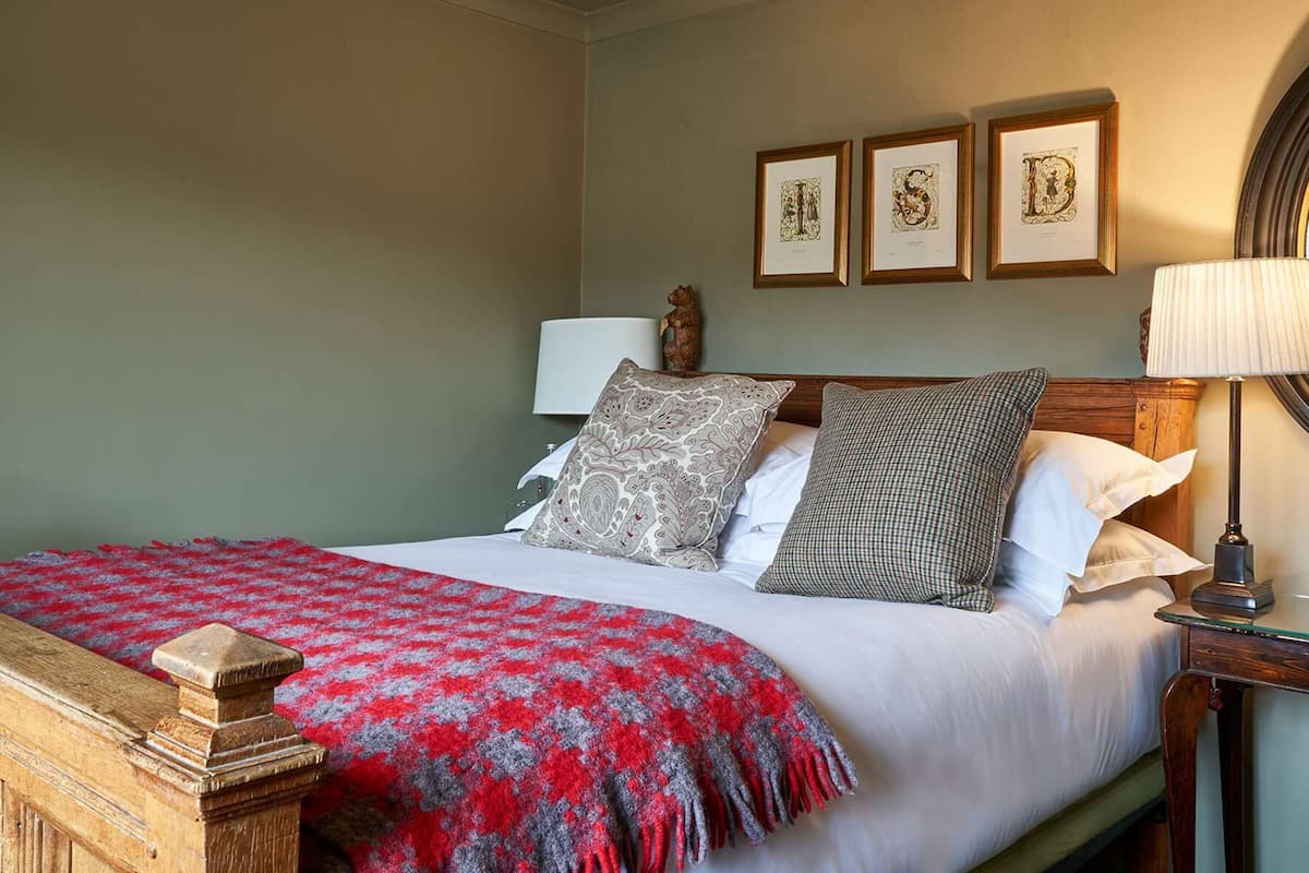 A neatly made bed with a red and grey blanket, a wooden headboard, and three framed artworks above it.