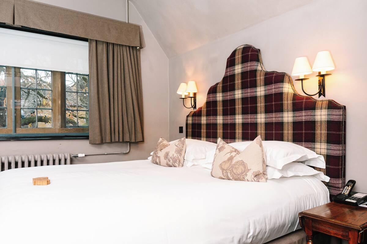 A neatly made bed with a plaid headboard, two wall-mounted lamps, and a bedside table with a telephone.