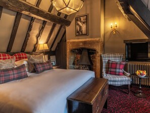 A cozy room with a bed, a fireplace, a television, and a small table with fruit. - The Lygon Arms (Broadway)