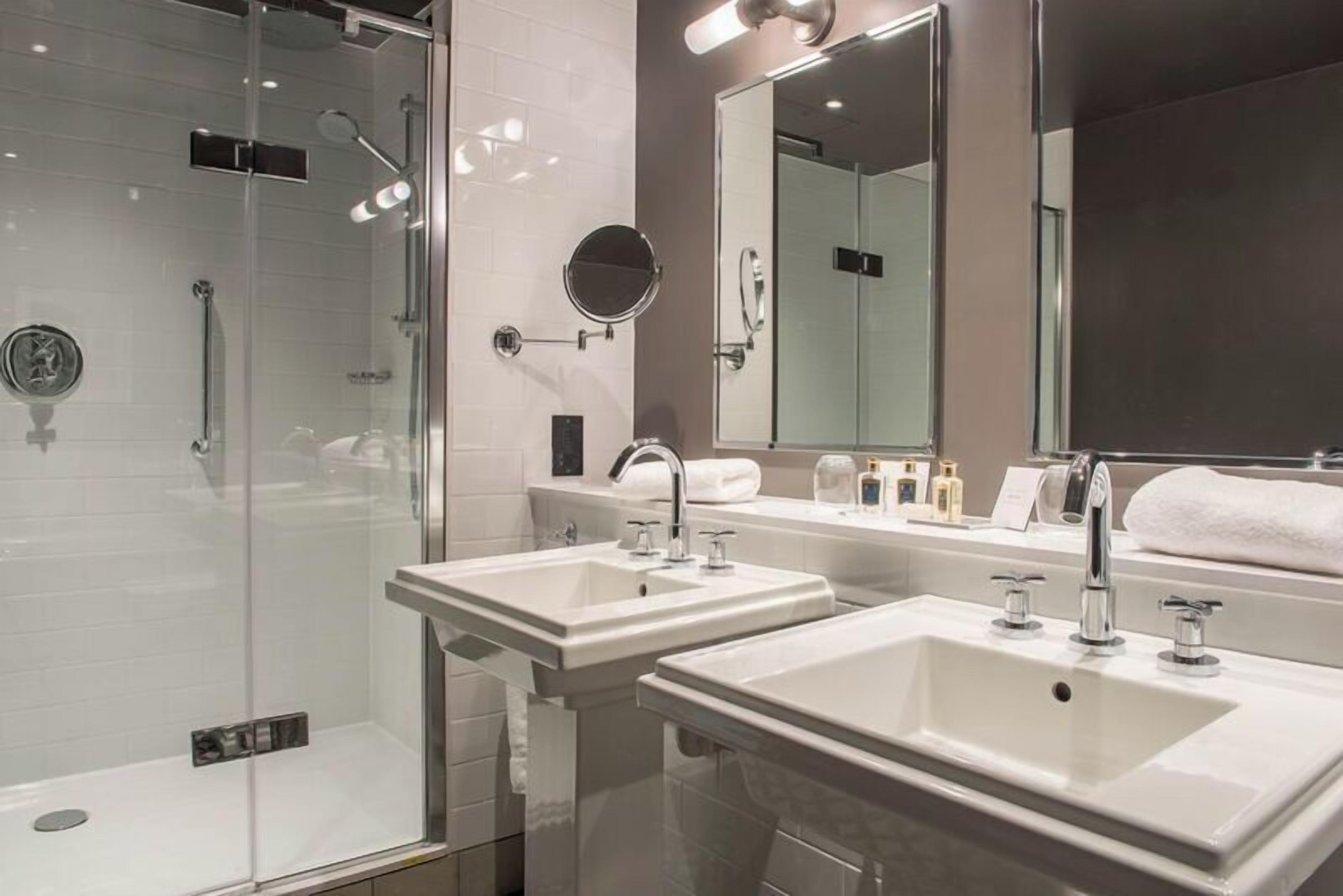 Un baño moderno con dos lavabos, cabina de ducha de vidrio y un espejo grande.