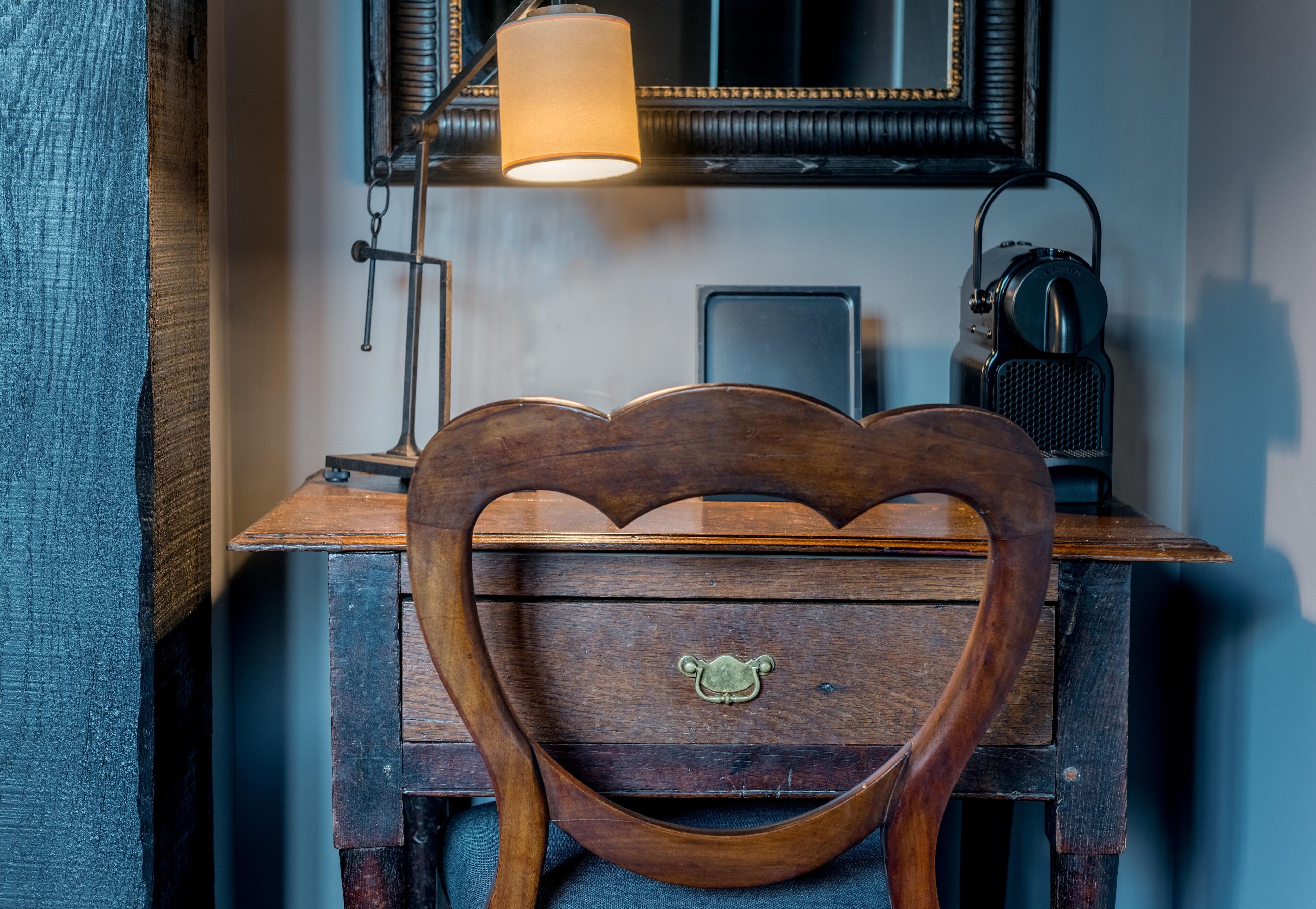 Una silla de madera con un respaldo en forma de corazón y un asa de latón, ubicada frente a un escritorio con una lámpara y un radio.