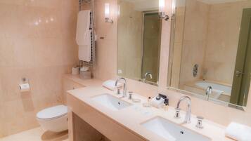 Un baño moderno con dos lavamanos, un inodoro y una ducha con mampara de vidrio.