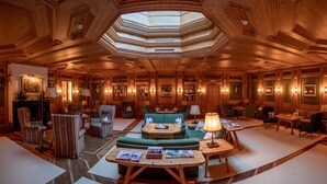 Un lobby espacioso con techo alto, paneles de madera, una zona de estar central con sofás y sillones, una chimenea y un tragaluz.