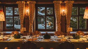 Un comedor cálidamente iluminado con una mesa dispuesta para cuatro, ventanas amplias con cortinas y vistas a un paisaje nevado.