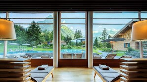 Un área de spa con tumbonas de madera, una piscina y vistas a la montaña.
