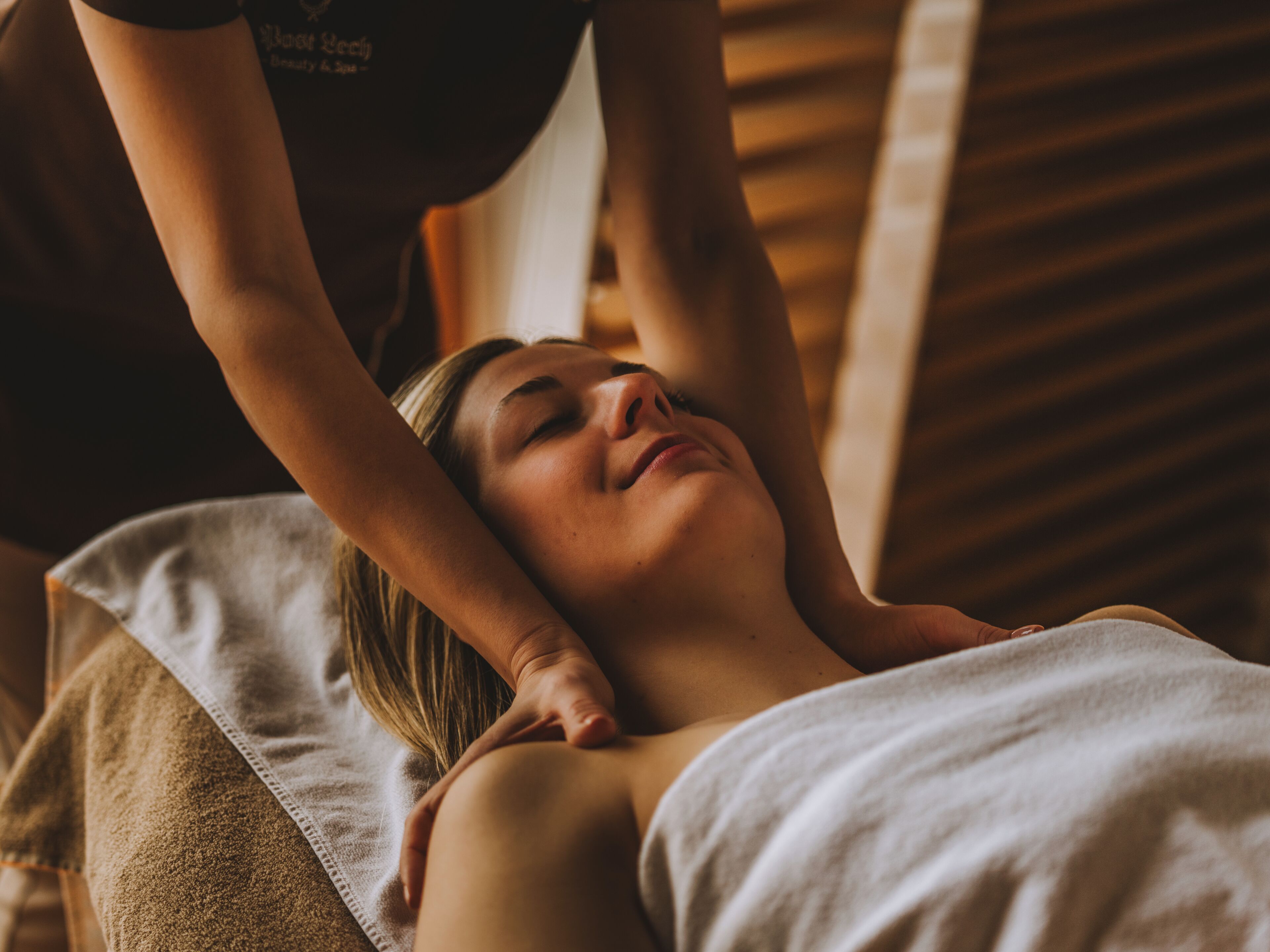 A person receiving a massage in a room with wooden paneling and a white towel.