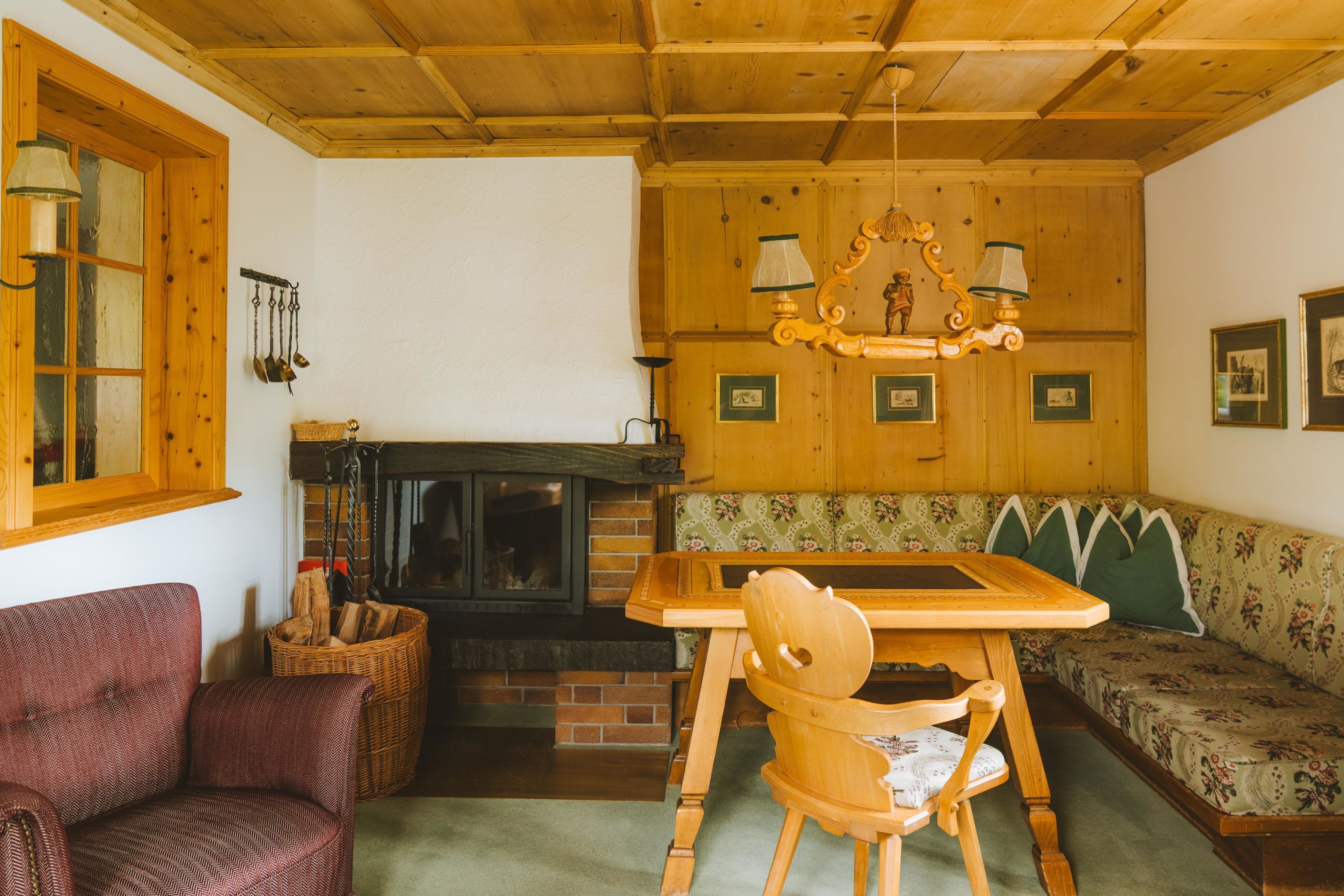 A cozy room with a wooden ceiling, a fireplace, a wooden table, a bench, and a chair.