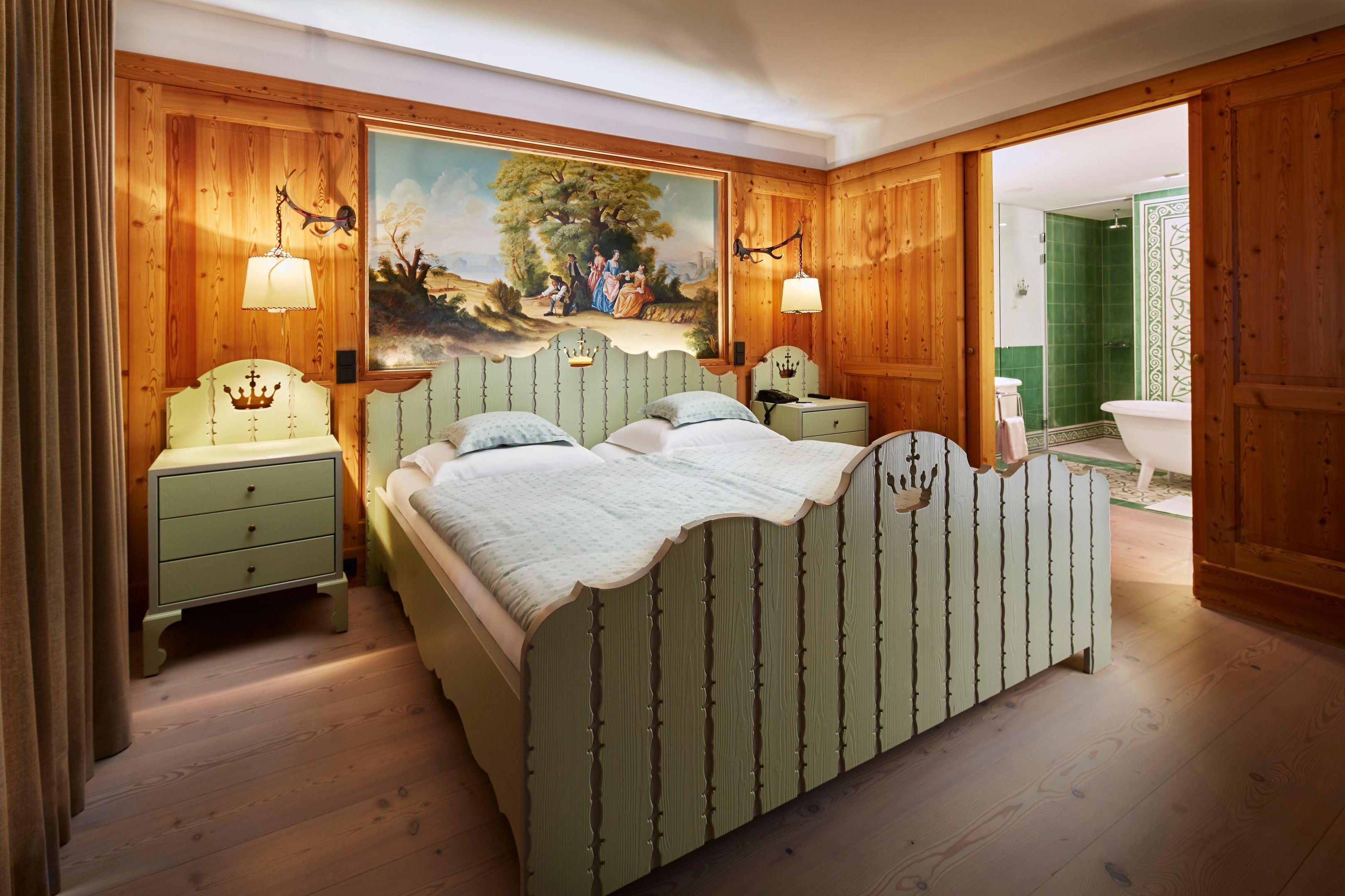 Une chambre avec un lit, des tables de chevet, un tableau et une salle de bain visible à travers une porte ouverte.
