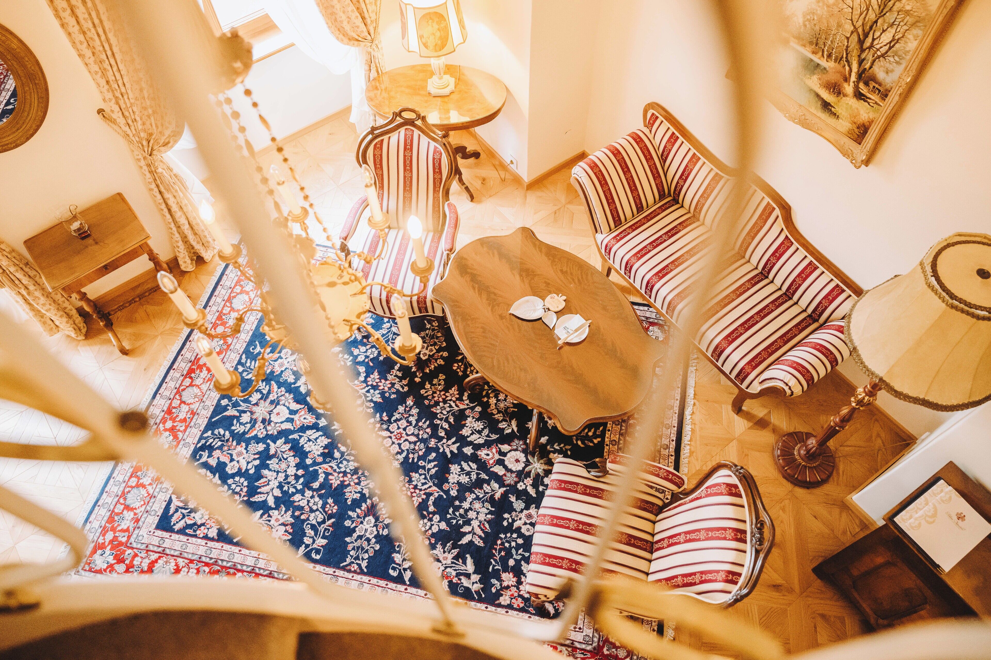 A room with a round wooden table, striped sofas, a patterned rug, and a chandelier.