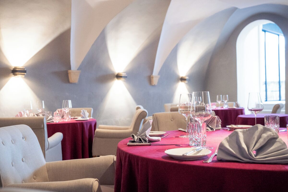 A restaurant with round tables set for dining, featuring a red tablecloth and white napkins.