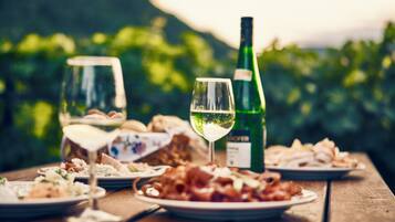 A wooden table with plates of food and wine glasses, set outdoors with a blurred green background.