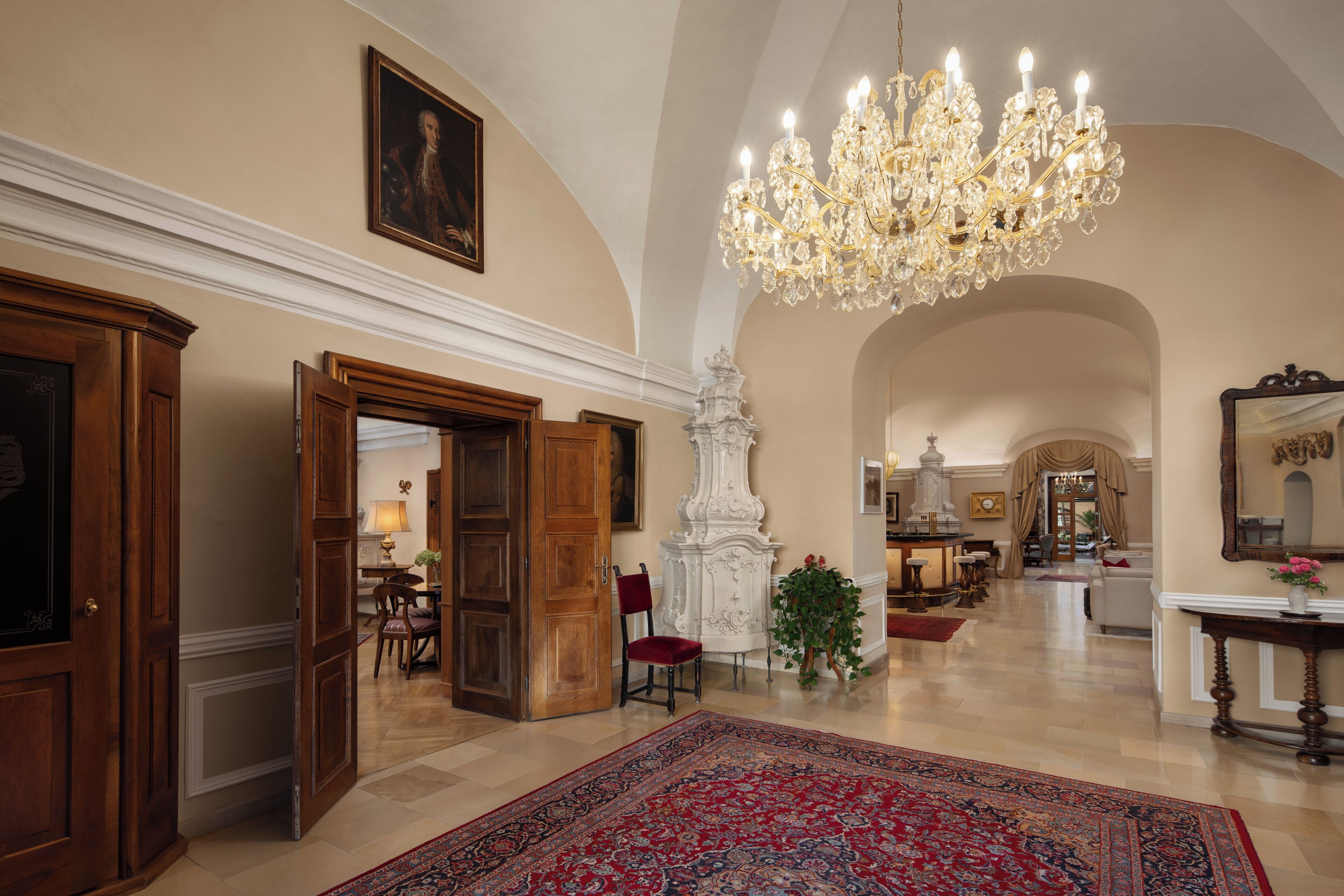 A spacious lobby with a grand chandelier, wooden doors, and a large rug.