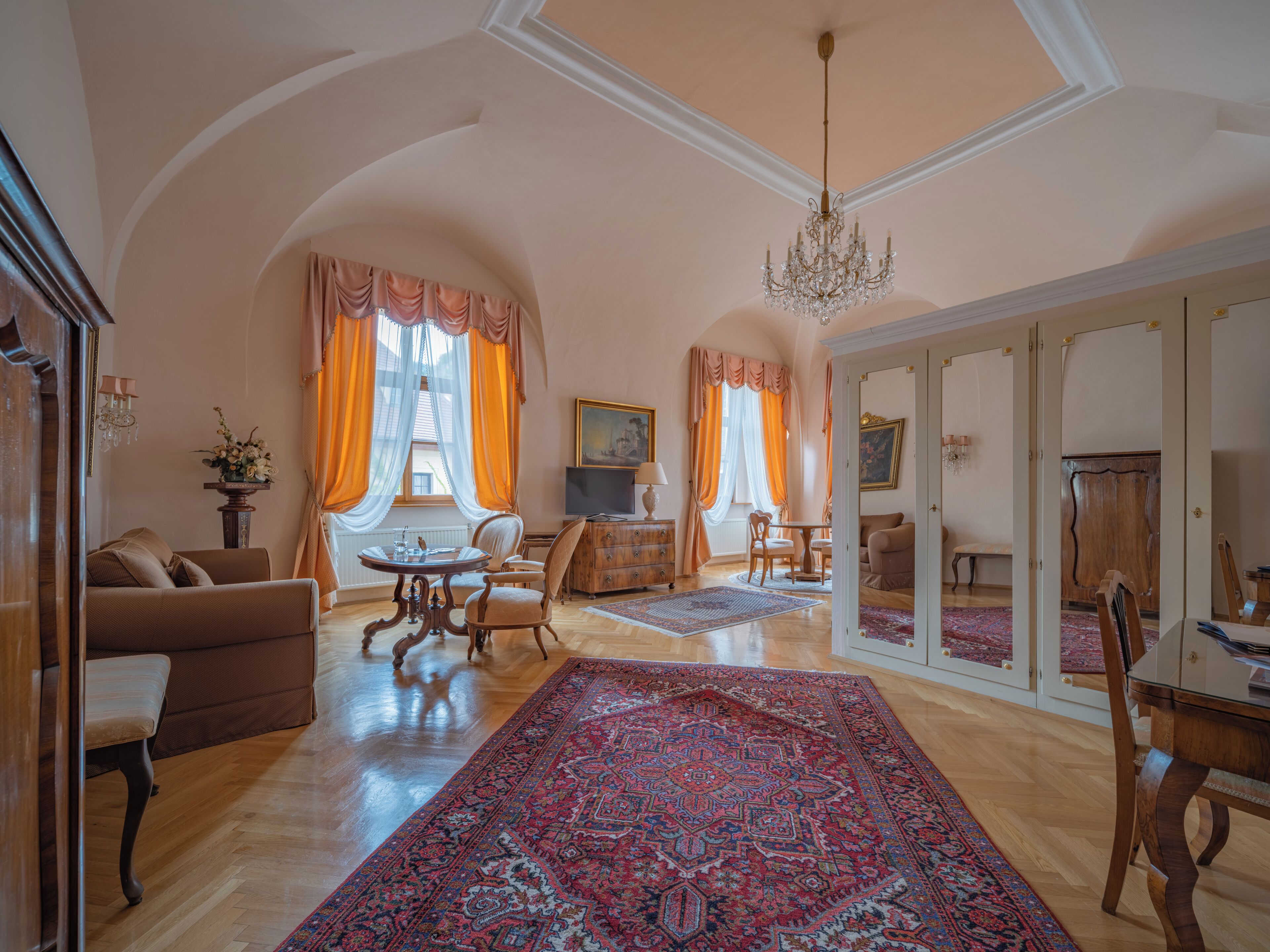 Uma sala de estar ampla com um tapete grande, um candelabro e uma televisão.