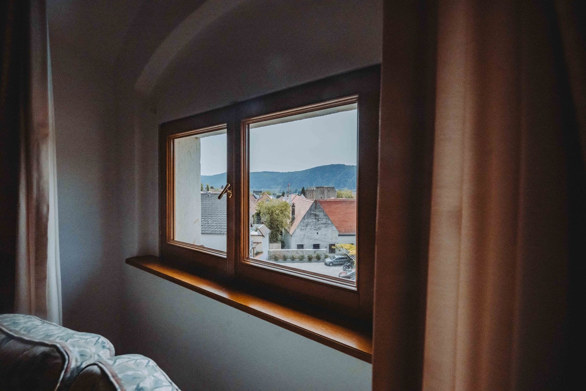 A room with a window overlooking a town and mountains.