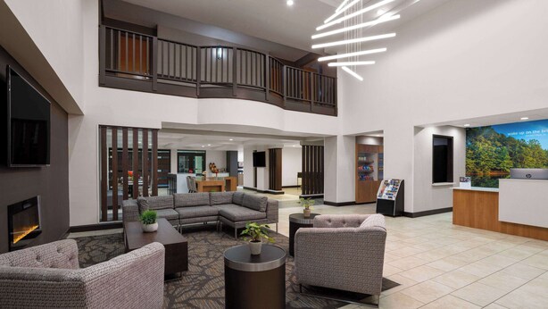 A spacious lobby with a modern design, featuring a seating area with sofas and a coffee table, a reception desk, and a staircase to an upper level.