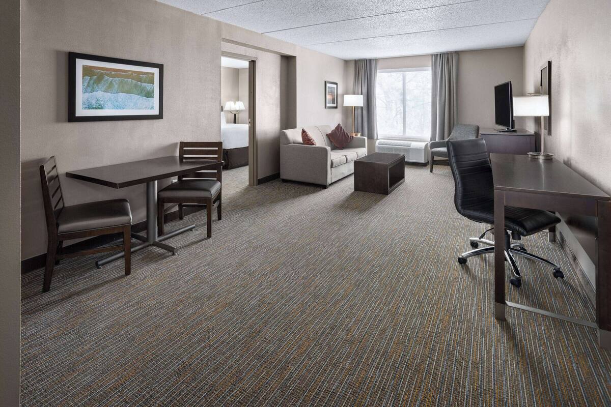 A hotel room with a sofa, a dining table, a TV, and a desk.