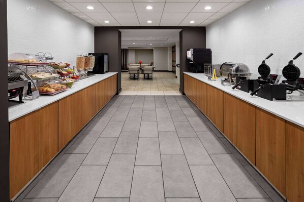 Un área de cocina moderna con mesas de buffet, diversas estaciones de comida y una máquina de café.