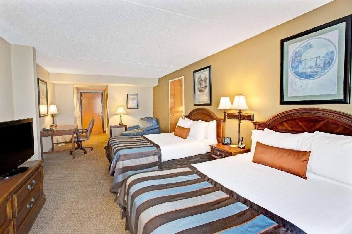 A hotel room with four beds, a desk with a chair, a television, and framed artwork on the walls.