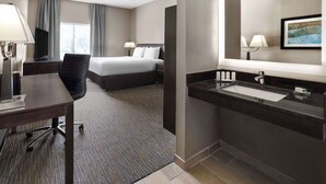 A hotel room with a bed, desk, chair, and a bathroom with a sink and mirror.