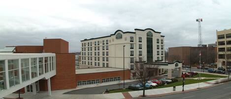 A hotel with a prominent entrance, a parking lot, and a clear sky.