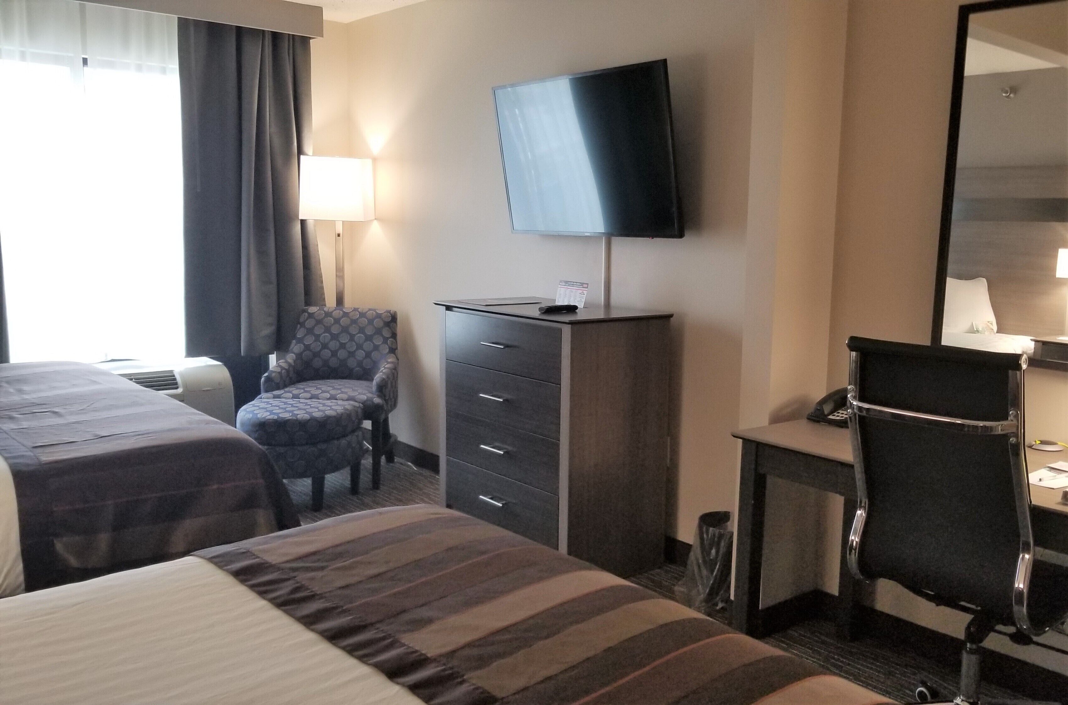 A hotel room with two beds, a desk, a chair, a television, and a mirror.