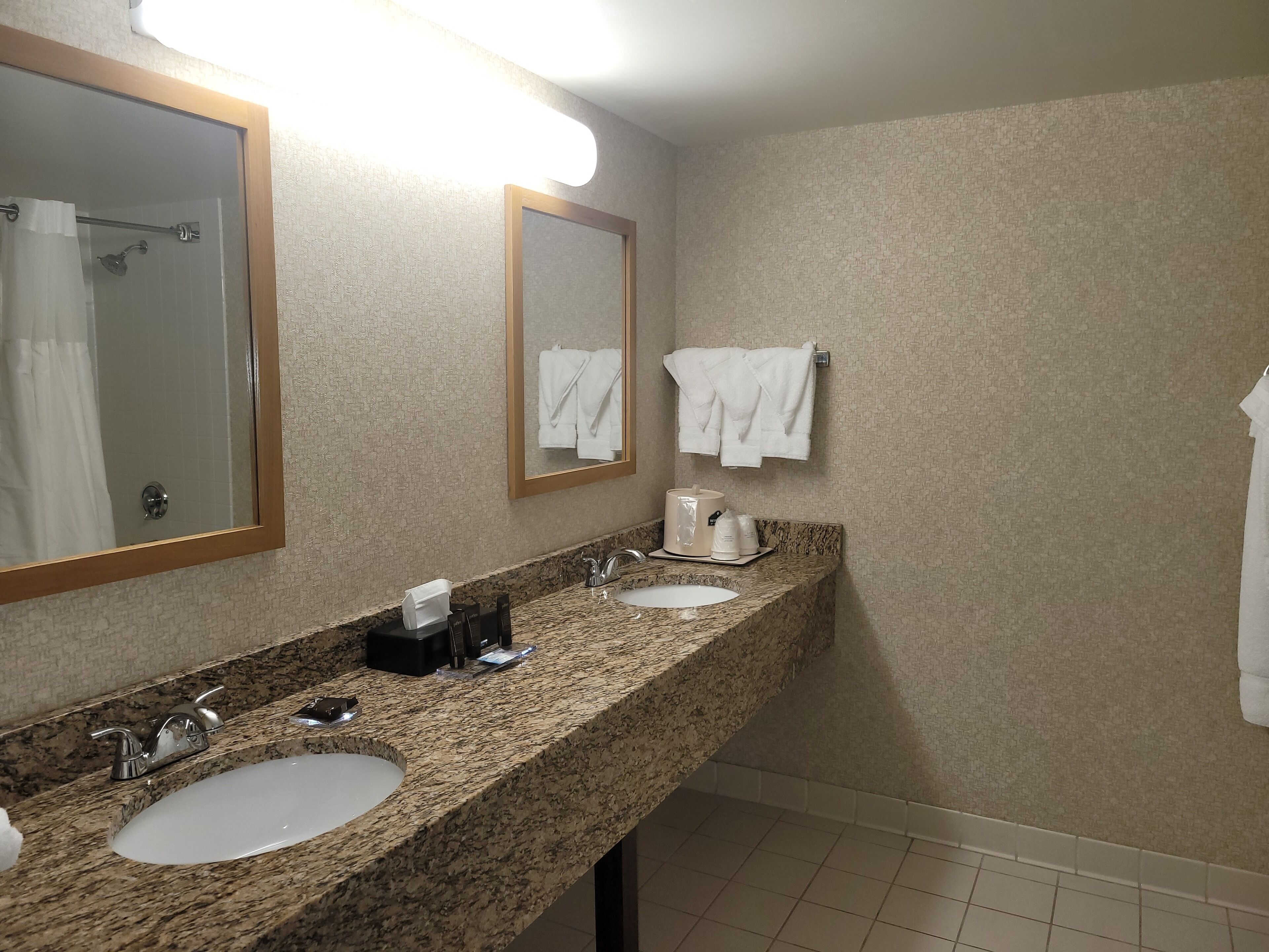 A hotel bathroom with two sinks, a shower, and a towel rack.