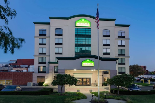 A Wingate Inn hotel with a modern design, featuring a prominent green and white color scheme, large windows, and a well-lit entrance.