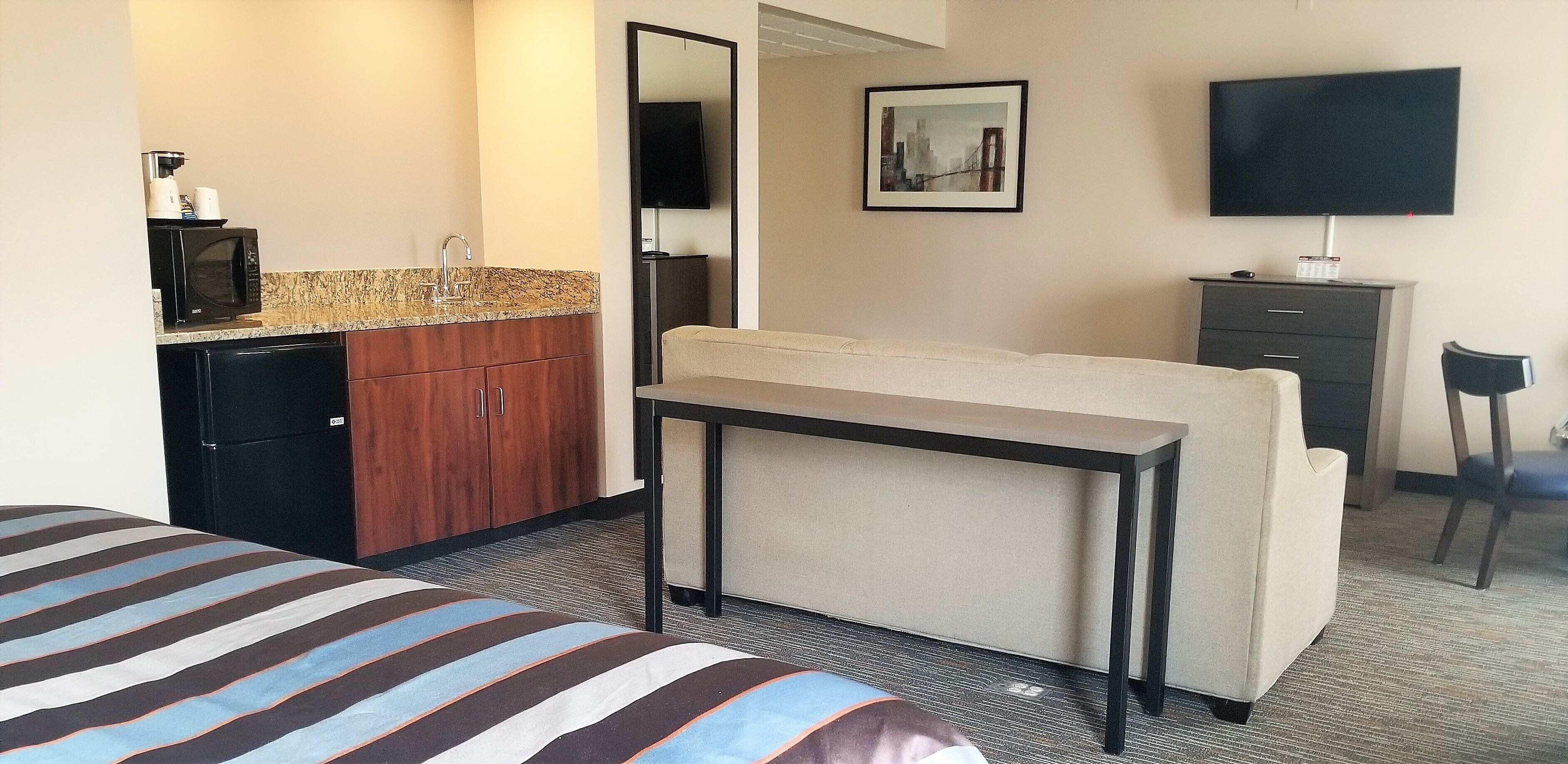 A hotel room with a bed, a small kitchenette with a microwave, a coffee maker, and a TV.