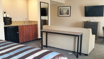 A hotel room with a bed, a small kitchenette with a microwave, a coffee maker, and a TV.