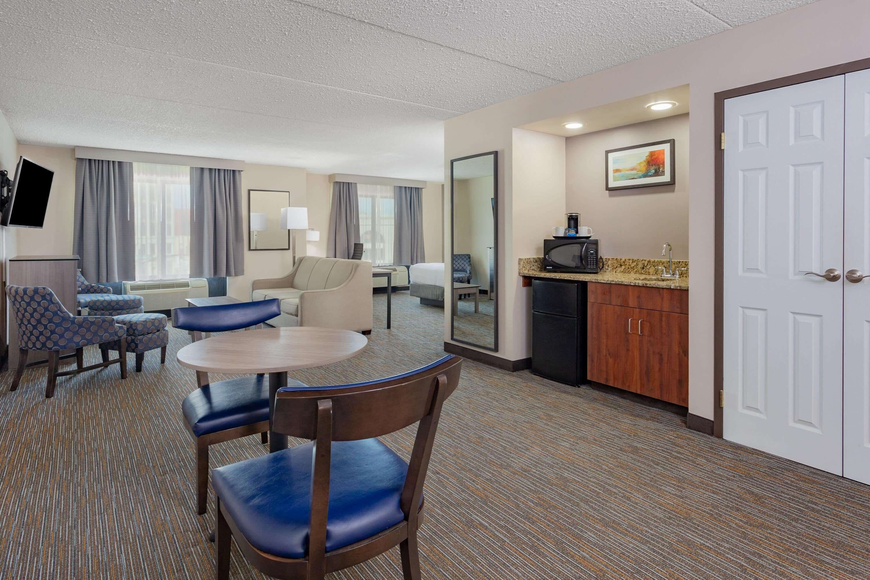 A hotel room with a dining area, a sofa, a TV, and a kitchenette.