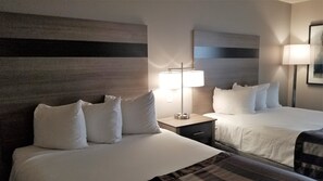 A hotel room with two beds, a nightstand, a lamp, and a wall-mounted mirror.