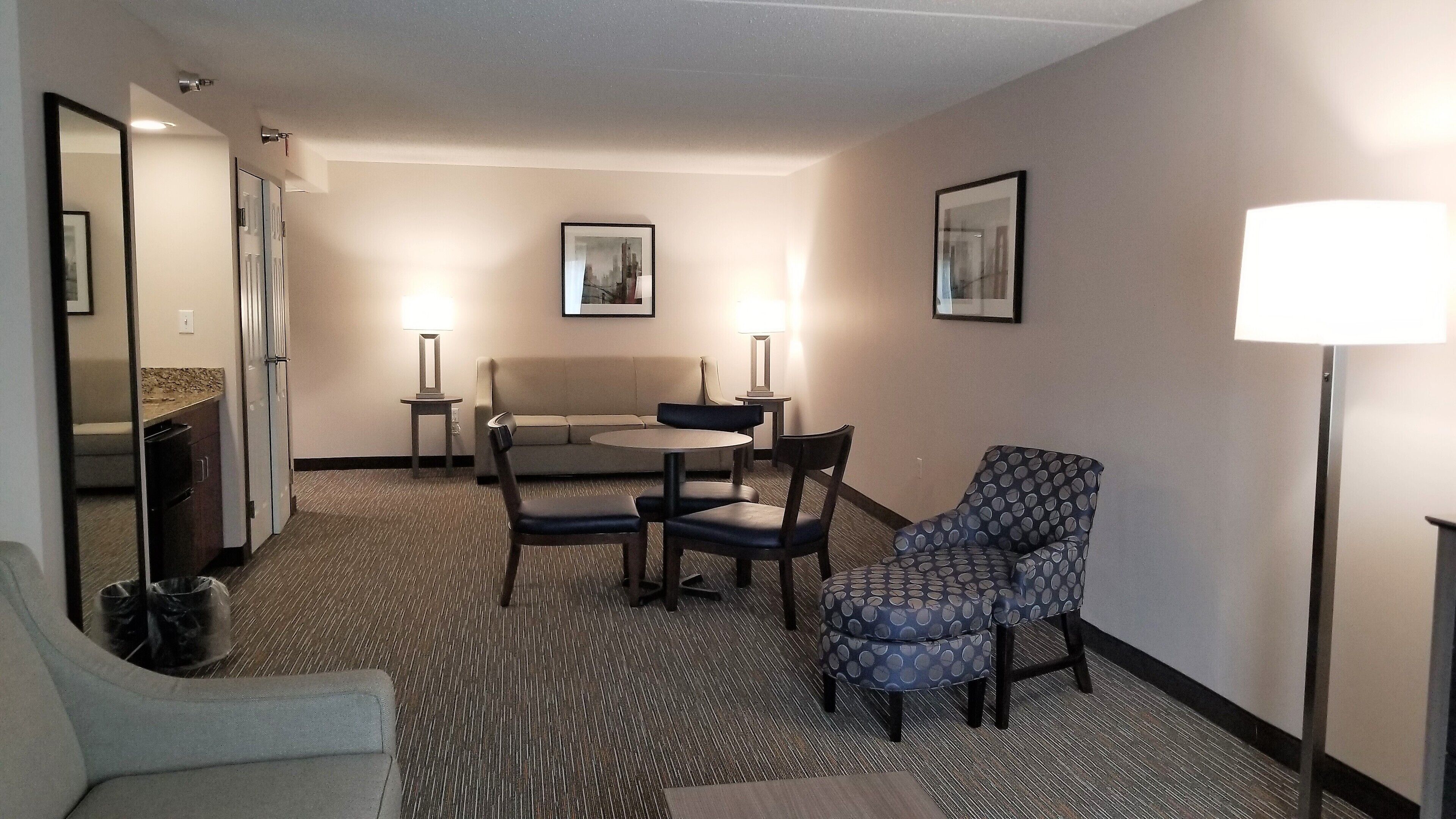 A hotel room with a sofa, two chairs, a small table, a lamp, and a picture on the wall.