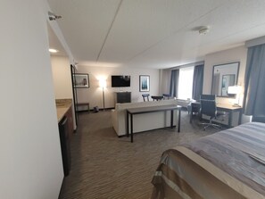A hotel room with a bed, a desk, a chair, a TV, and a lamp.
