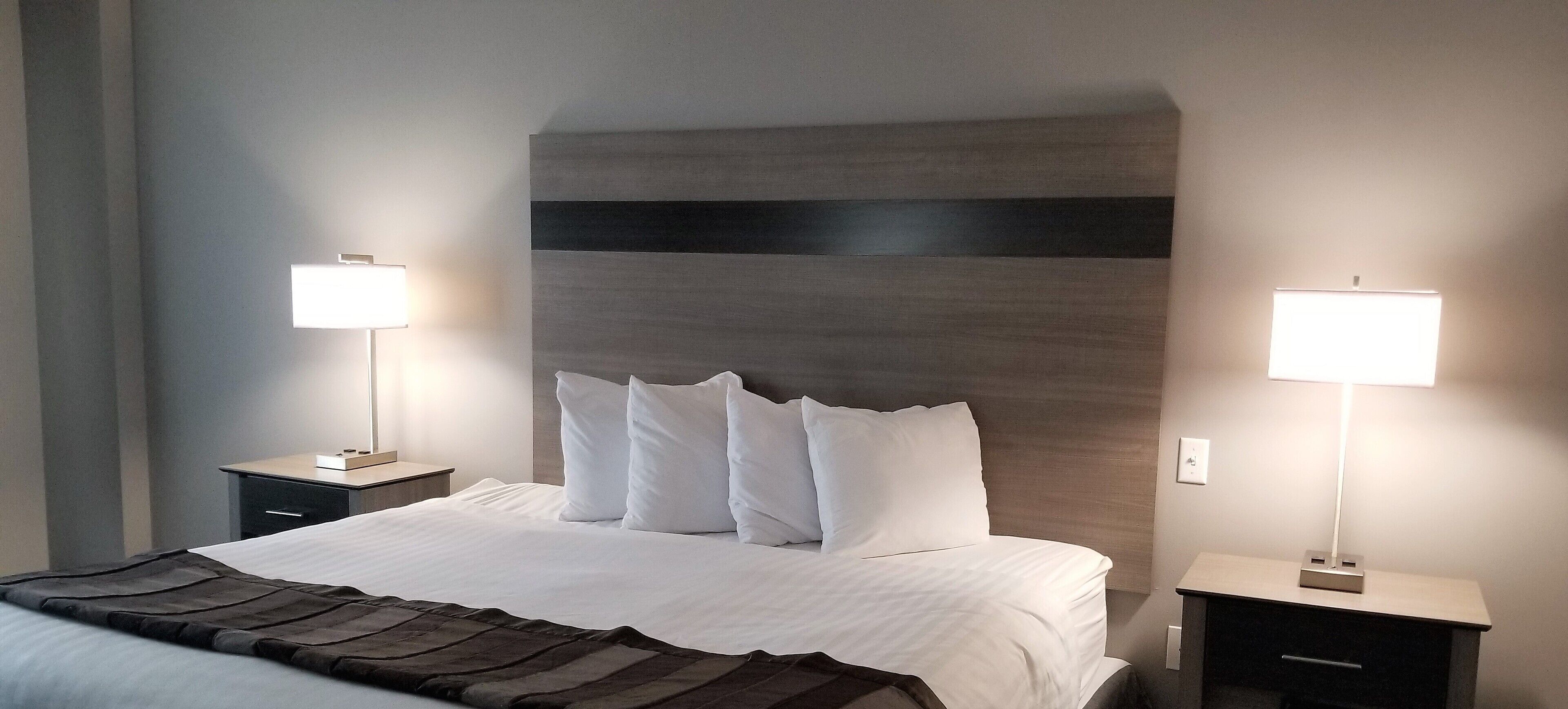 Una habitación de hotel con una cama grande, dos mesitas de noche y dos lámparas fijadas a la pared.