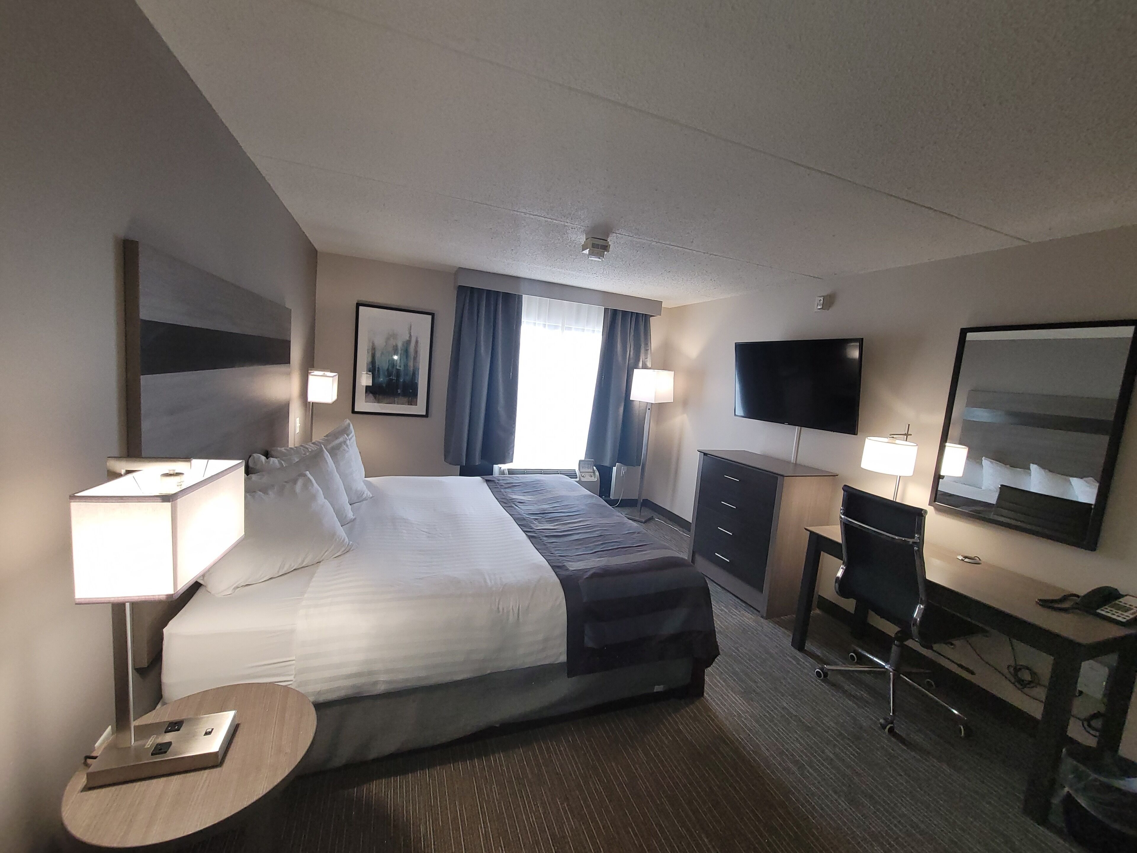 Une chambre d’hôtel dotée d’un grand lit, de tables de chevet avec des lampes, d’un bureau avec une chaise, d’un téléviseur à écran plat et d’un grand miroir.