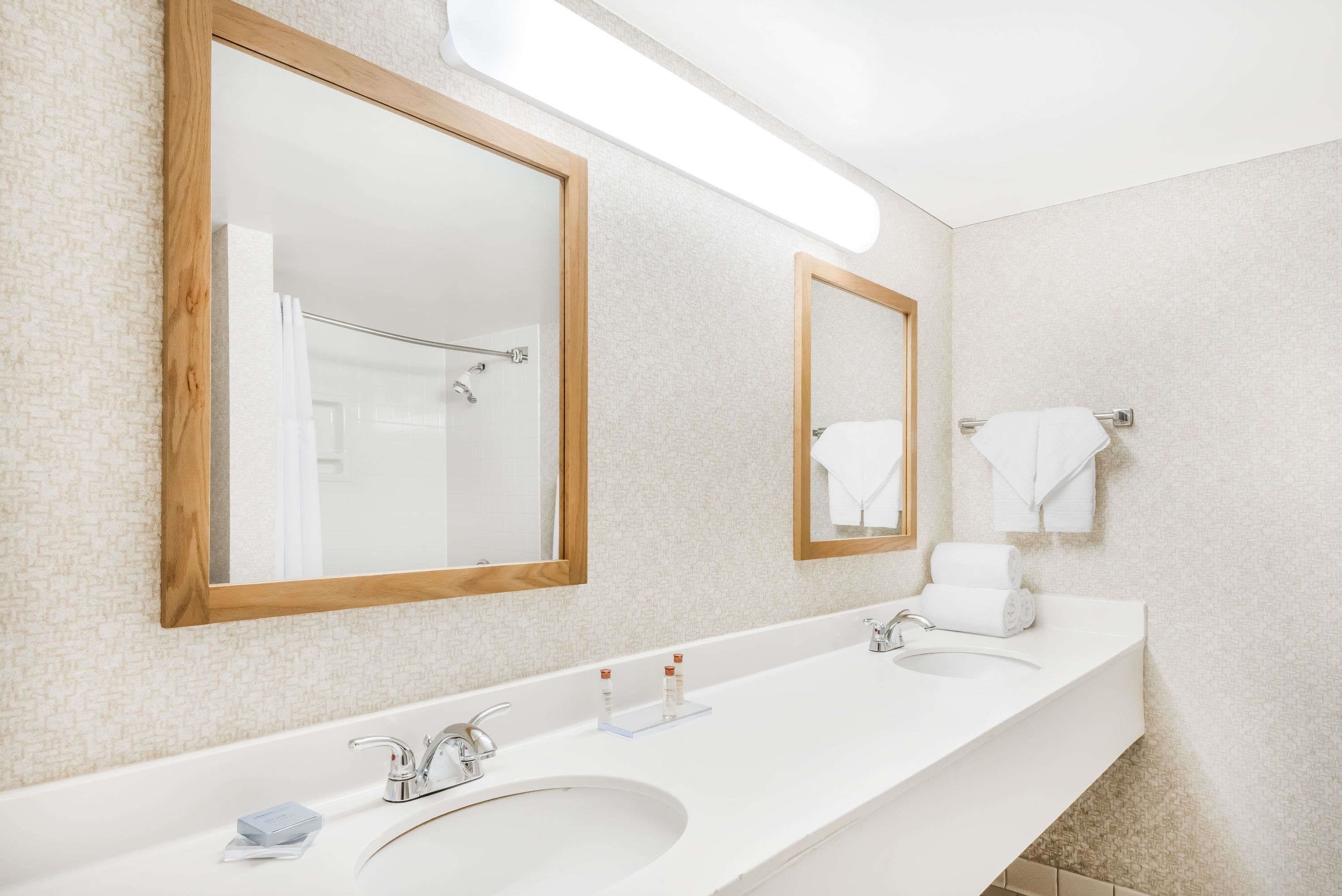 Un baño moderno con dos lavamanos, espejos con marco de madera y un perchero para toallas.