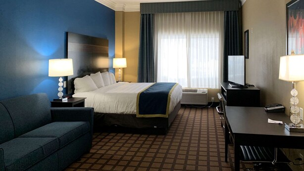 A hotel room with a bed, two bedside tables with lamps, a desk with a chair, a couch, and a large window with curtains. - Comfort Inn Saint Paul East (Oakdale)