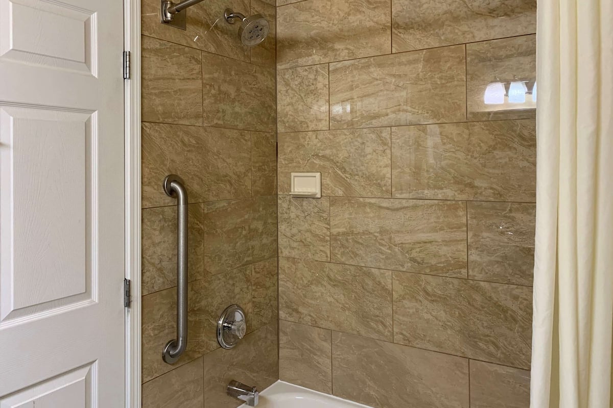 A bathroom with a shower, grab bars, and a bathtub.