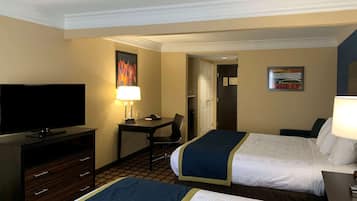 A hotel room with two beds, a desk with a lamp, a television, and a door leading to another room.